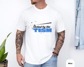 Photo 4 of 8: White vintage wash tee worn by a tattooed man, featuring playful Touched by the TISM lettering in bold blue and black, a funny autism shirt with cozy modern style and a witty gift feel for neurodivergent shirt fans and ASD awareness gift shoppers