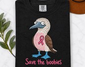 Photo 6 of 17: A folded black t-shirt printed with a blue-footed booby bird graphic, pink ribbon, and the text Save the boobies.