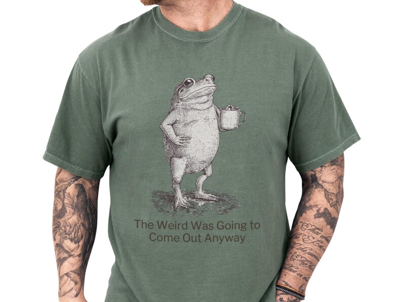 Relaxed moss green unisex t shirt featuring a vintage sketch frog holding a coffee mug and the witty slogan 'The Weird Was Going to Come Out Anyway', a funny frog shirt and frog graphic tee with quirky humor and introvert humor vibes, cozy gift for him