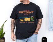 Photo 5 of 10: Outdoor lifestyle shot of a man on a bike wearing a unisex funny shirt — a pixel art tshirt with a playful "please be patient t" aging humor slogan referencing born in the 1900s, retro gaming colors and cozy vintage cotton, perfect Gen X or millennial gag gift