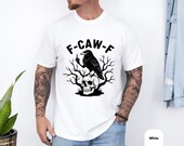 Photo 4 of 8: Male model wearing a white unisex crow pun tshirt with a bold black raven graphic perched on a skull among bare branches, crow flipping a rude wing for dark humor, gothic crow shirt and skull bird tee with edgy graphic tee energy, sarcastic tee and f caw f shirt ideal as gifts for men