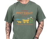 Photo 3 of 10: Man wearing soft faded black unisex tee with pixel art covered wagon, mountains and trees and bold retro text reading 'Please Be Patient With Me I Was Born In The 1900s', a funny retro tee with aging humor and gamer-style nostalgia, cozy vintage look perfect gift for millennial or Gen X