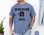 Photo 6 of 8: Casual blue jean t-shirt worn by a male model showing a bold black kettle-smoker icon and cheeky slogan about animals harmed for this smoke, a bbq humor shirt and dark humor tee with rustic smoky vibes, perfect funny grill shirt or meat smoker gift for the grillmaster, dad, or grilling enthusiast
