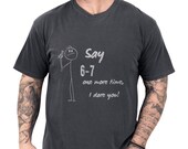 Photo 1 of 8: Charcoal minimalist stick figure tee showing a hand‑drawn stick man and cheeky script saying Say 6‑7 one more time I dare you, worn by a casually tattooed model — playful, youthful casual tee perfect as a teacher gift tee, parent gag gift shirt, or humorous gift for teacher appreciation