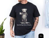 Photo 3 of 8: Folded charcoal unisex t shirt on a rustic wood surface featuring a distressed opossum illustration holding a coffee mug, sly and slightly spooky for fans of animal humor, a funny opossum tee with sarcastic t shirt and dark humor vibes, a novelty graphic tee gift for him or introvert who loves passive aggressive spite humor and possum meme shirt