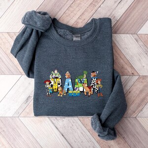 May include: A dark gray sweatshirt featuring the word "MAX" with colorful cartoon characters. The letters are decorated with images of characters from a popular animated movie. The sweatshirt has a crew neck and long sleeves.