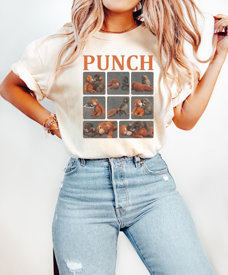 May include: Cream-colored t-shirt with the word "PUNCH" in orange block letters. Below the text are nine small squares, each containing a vintage-style illustration of teddy bears in various poses. The shirt is paired with light blue jeans.