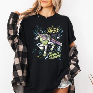 May include: Black t-shirt featuring a graphic of Buzz Lightyear in his space suit, with the text "Buzz Lightyear" and "To Infinity and Beyond" in a colorful design. The shirt is a casual wear item.
