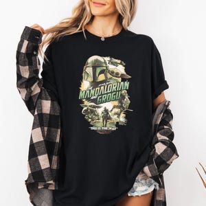 Puede incluir: Camiseta negra con un dise&ntilde;o gr&aacute;fico de la serie "The Mandalorian and Grogu". El dise&ntilde;o incluye im&aacute;genes del casco del Mandaloriano, Grogu y el texto "THIS IS THE WAY".