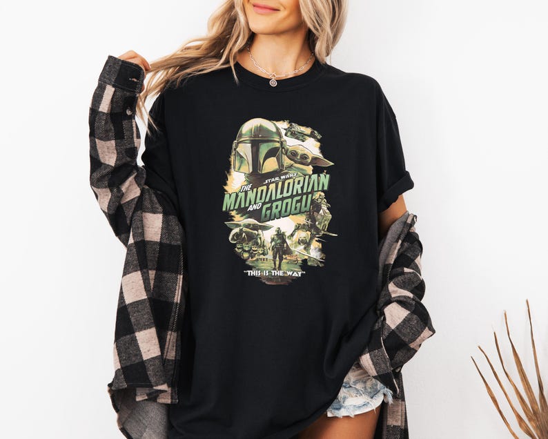 Puede incluir: Camiseta negra con un dise&ntilde;o gr&aacute;fico de la serie "The Mandalorian and Grogu". El dise&ntilde;o incluye im&aacute;genes del casco del Mandaloriano, Grogu y el texto "THIS IS THE WAY".