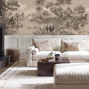 Op de afbeelding: Een gezellige woonkamer met een open haard en een hoekbank. De open haard is gemaakt van donker hout en heeft een brandend vuur. De muur achter de bank toont een sepia-getinte muurschildering van olifanten en een landschap.