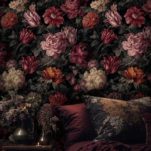 May include: A bedroom scene featuring a dark floral wallpaper with large, colorful flowers in shades of red, pink, and cream. The bed has burgundy bedding, a patterned pillow, and a knitted throw. A small table holds vases and a lit candle.