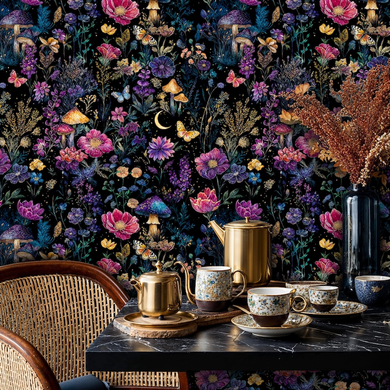 May include: A colourful floral wallpaper with a dark backdrop, showcasing flowers, mushrooms, and butterflies. A gold teapot, teacups, and saucers are arranged on a black table. A wicker chair and a vase with dried flowers are also visible.