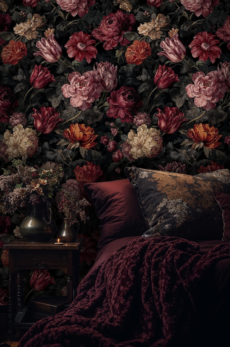 May include: A bedroom scene featuring a dark floral wallpaper with large, colorful flowers in shades of red, pink, and cream. The bed has burgundy bedding, a patterned pillow, and a knitted throw. A small table holds vases and a lit candle.