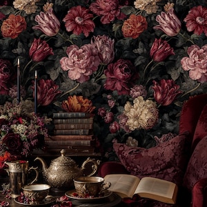 May include: A dark, floral wallpaper background with large, detailed flowers in shades of red, pink, and cream. A table is set with a gold teapot, cups, and a stack of books. A red armchair and open book complete the scene.