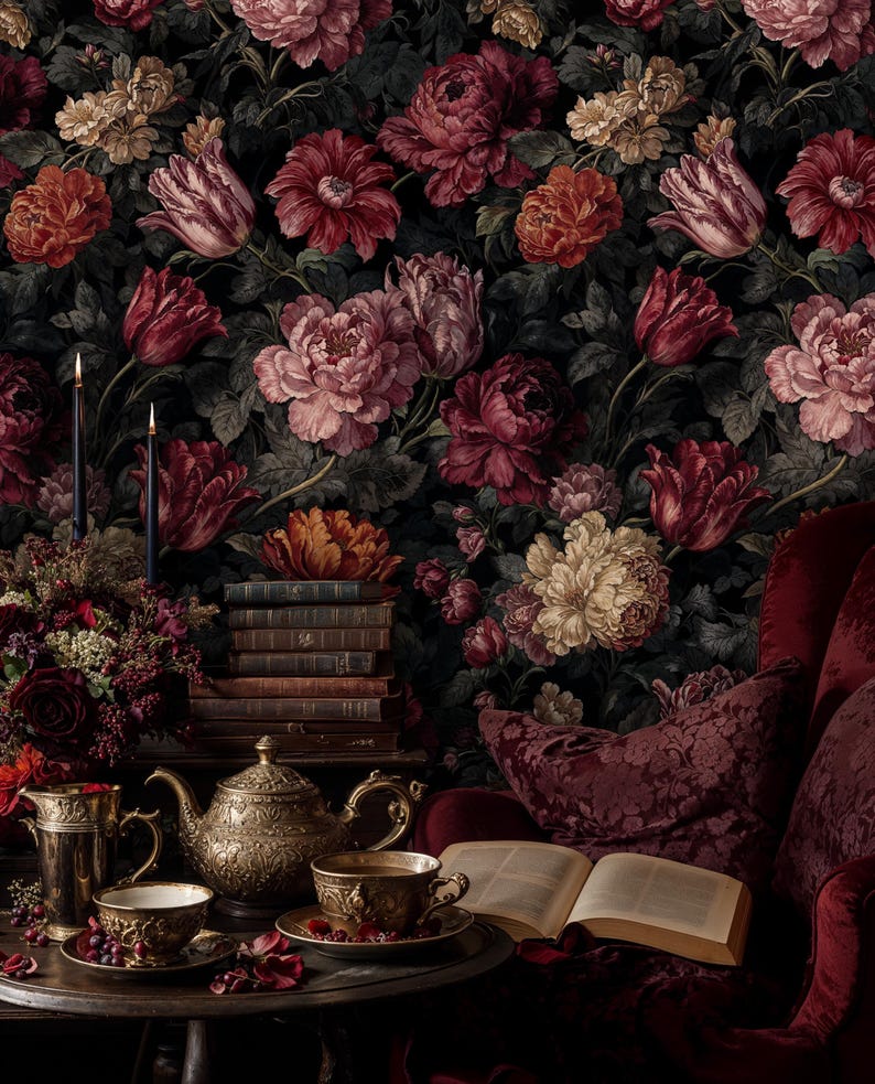May include: A dark, floral wallpaper background with large, detailed flowers in shades of red, pink, and cream. A table is set with a gold teapot, cups, and a stack of books. A red armchair and open book complete the scene.