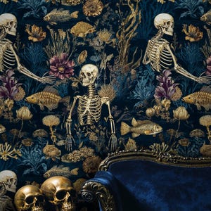K&ouml;nnte beinhalten: Dunkelblaue Tapete mit einem sich wiederholenden Muster aus Skeletten, Fischen und floralen Elementen in Gold und Lila. Zwei goldene Totenk&ouml;pfe stehen auf einem kleinen Tisch vor einem blauen Samtsessel.
