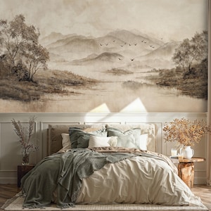 May include: A bedroom with a mural depicting a misty mountain landscape in brown and beige tones. The bed has a beige duvet, green throw, and various pillows. A wooden side table displays a vase and candles.