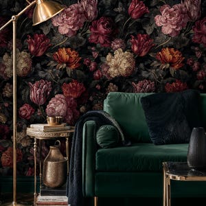 May include: A living room scene featuring a dark floral wallpaper with large blooms in shades of red, pink, and orange. A green velvet sofa with black pillows sits in front of the wallpaper. A gold floor lamp and side table add to the room's decor.