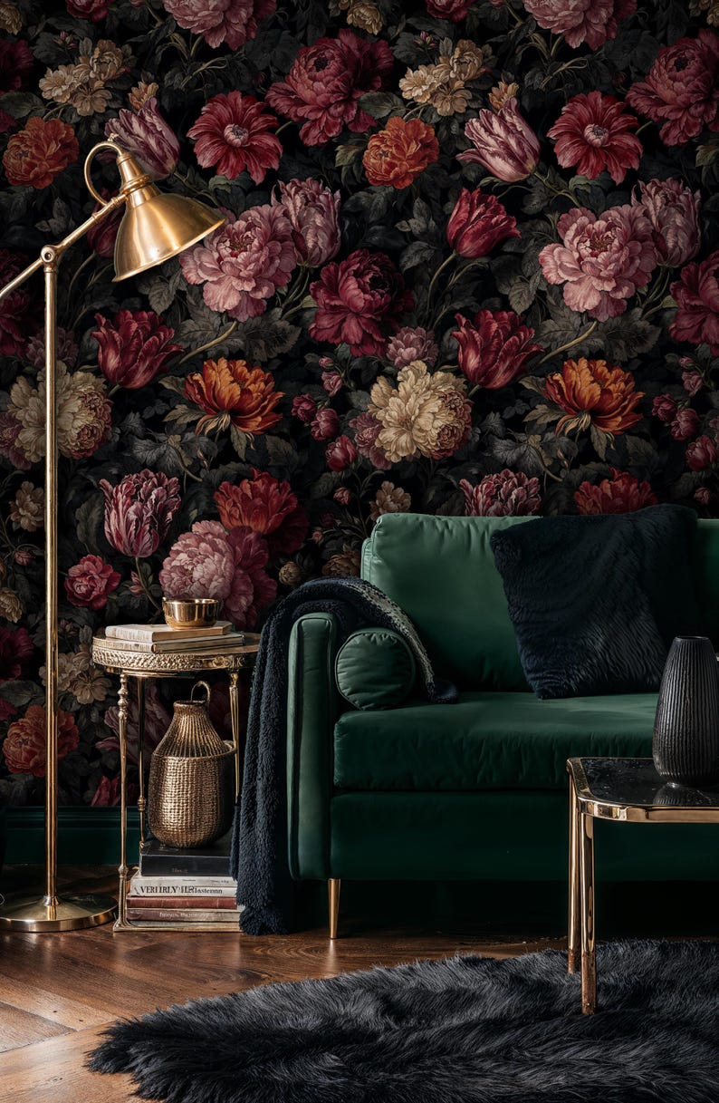 May include: A living room scene featuring a dark floral wallpaper with large blooms in shades of red, pink, and orange. A green velvet sofa with black pillows sits in front of the wallpaper. A gold floor lamp and side table add to the room's decor.