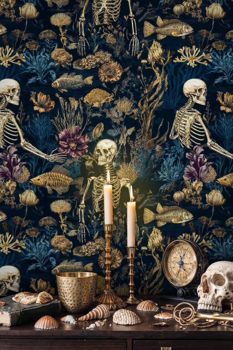 K&ouml;nnte beinhalten: Dunkelblaue Tapete mit einem sich wiederholenden Muster aus goldenen Skeletten, Fischen und floralen Elementen. Zwei brennende Kerzen in goldenen Haltern stehen vor der Tapete. Ein Totenkopf, ein Kompass und Muscheln liegen auf einer Holzoberfl&auml;che.