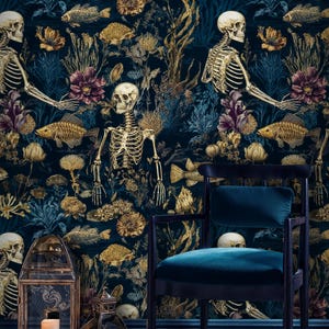 K&ouml;nnte beinhalten: Dunkelblaugr&uuml;ne Tapete mit einem sich wiederholenden Muster aus goldenen Skeletten, Fischen und floralen Elementen. Ein schwarzer Stuhl mit einem teal-farbenen Samtsitz steht vor der Tapete. Zwei goldene Laternen mit Kerzen stehen auf dem Boden.