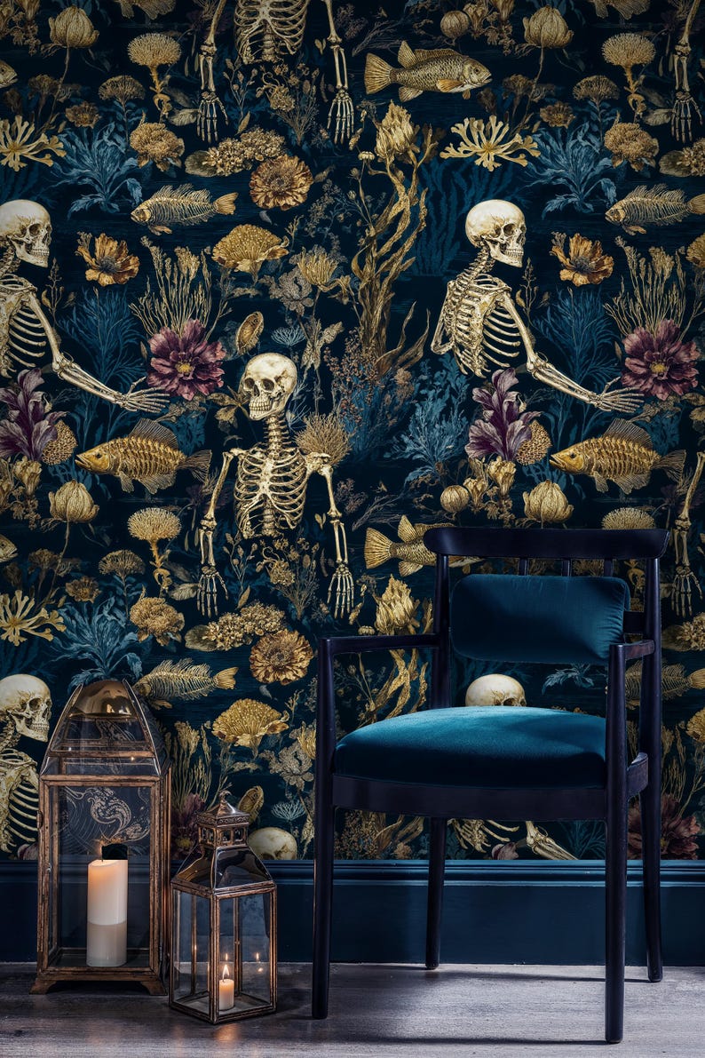 K&ouml;nnte beinhalten: Dunkelblaugr&uuml;ne Tapete mit einem sich wiederholenden Muster aus goldenen Skeletten, Fischen und floralen Elementen. Ein schwarzer Stuhl mit einem teal-farbenen Samtsitz steht vor der Tapete. Zwei goldene Laternen mit Kerzen stehen auf dem Boden.