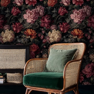 May include: A floral wallpaper featuring large, dark-toned blooms in shades of red, pink, and cream. A rattan armchair with a green velvet seat and a matching pillow sits in front of the wallpaper. A black cabinet with a woven front is to the left.