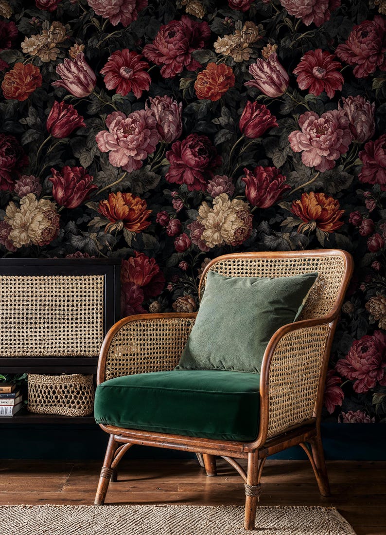 May include: A floral wallpaper featuring large, dark-toned blooms in shades of red, pink, and cream. A rattan armchair with a green velvet seat and a matching pillow sits in front of the wallpaper. A black cabinet with a woven front is to the left.