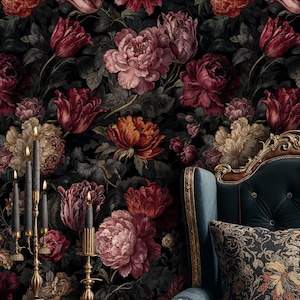 May include: A dark floral wallpaper featuring large, detailed flowers in shades of red, pink, and cream against a black background. A teal armchair with gold trim and a patterned pillow is in the corner. A gold candelabra with black candles and a glass of liquid are on a wooden table.