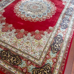 K&ouml;nnte beinhalten: Ein gro&szlig;er, verzierter roter Teppich mit einem zentralen Medaillon-Design. Der Teppich weist komplizierte Blumenmuster in Creme, Gold und Blau mit einem detaillierten Rand auf. Der Teppich ist rechteckig und scheint aus einem weichen Material zu bestehen.
