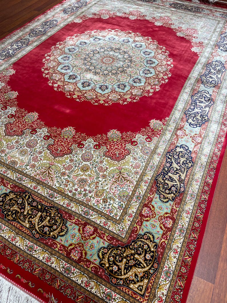 K&ouml;nnte beinhalten: Ein gro&szlig;er, verzierter roter Teppich mit einem zentralen Medaillon-Design. Der Teppich weist komplizierte Blumenmuster in Creme, Gold und Blau mit einem detaillierten Rand auf. Der Teppich ist rechteckig und scheint aus einem weichen Material zu bestehen.
