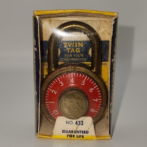 May include: Vintage combination lock in its original box. The lock has a red dial with white numbers and a brass-colored body. The box reads "TWIN TAG" and "GUARANTEED FOR LIFE".