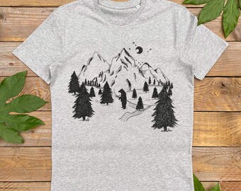 May include: A heather gray t-shirt featuring a black and white illustration of a mountain scene with trees, a bear, and a crescent moon. The graphic design is centered on the front of the shirt, creating a nature-themed aesthetic.