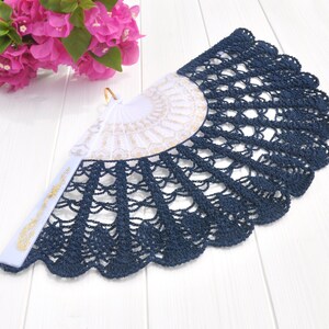 May include: A navy blue crocheted fan with a white and gold lace design. The fan is closed and has a white handle.