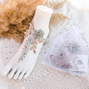 May include: A pair of delicate, floral ankle jewelry with a light blue and brown design. The jewelry is made of lace and features a floral pattern with small beads. The jewelry is displayed on a white mannequin foot.
