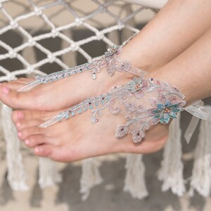 May include: A pair of delicate, floral-embellished foot jewelry with silver and blue accents. The jewelry is made of lace and features a floral design with rhinestones.
