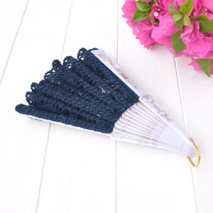 May include: A blue and white hand fan with a lace trim. The fan is closed and has a gold handle.