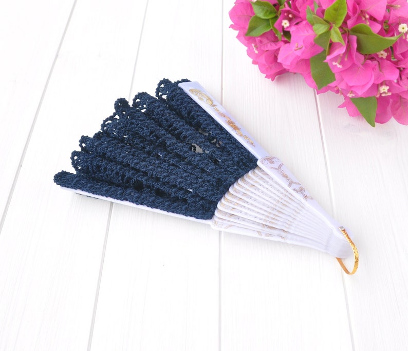 May include: A blue and white hand fan with a lace trim. The fan is closed and has a gold handle.