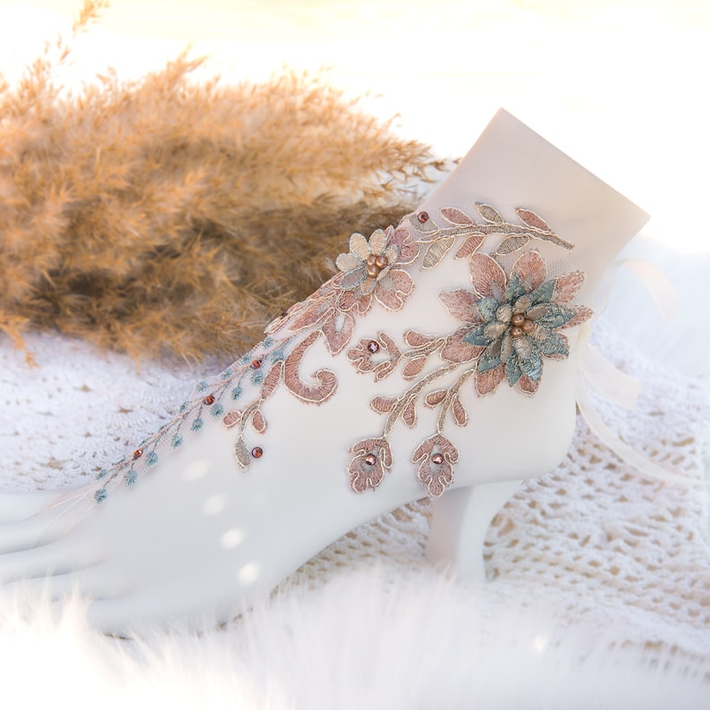 May include: A white shoe with a delicate floral design in shades of brown and blue. The design features intricate embroidery and small beads.