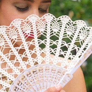 May include: A white crocheted fan with a gold-coloured handle. The fan is closed and held by a person.