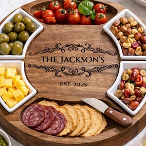 Könnte beinhalten: Ein runder Servierteller aus Holz mit mehreren Fächern, die mit Snacks gefüllt sind. Das Tablett enthält Oliven, Käsewürfel, Tomaten, Nüsse, Salami und Cracker. Das Tablett ist mit "THE JACKSON'S EST. 2025" graviert.