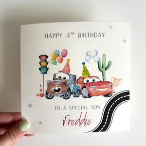 Peut inclure: Une carte de vœux d'anniversaire carrée avec des illustrations à l'aquarelle de deux voitures de dessin animé portant des chapeaux de fête, un feu de signalisation, un cactus, des ballons et un trophée. Le texte indique HAPPY 4TH BIRTHDAY TO A SPECIAL SON Freddie.