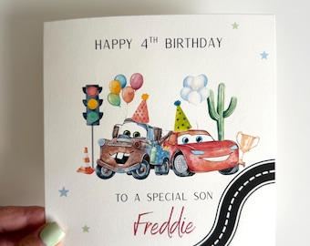 Peut inclure: Une carte de vœux d'anniversaire carrée avec des illustrations à l'aquarelle de deux voitures de dessin animé portant des chapeaux de fête, un feu de signalisation, un cactus, des ballons et un trophée. Le texte indique HAPPY 4TH BIRTHDAY TO A SPECIAL SON Freddie.