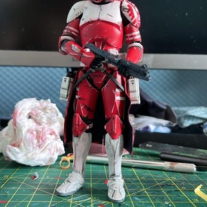 Pu&ograve; includere: Action figure rossa e bianca di un clone trooper di Star Wars. La figura &egrave; in piedi, con un fucile blaster nero. Indossa un elmetto, un'armatura e stivali. Lo sfondo &egrave; sfocato.