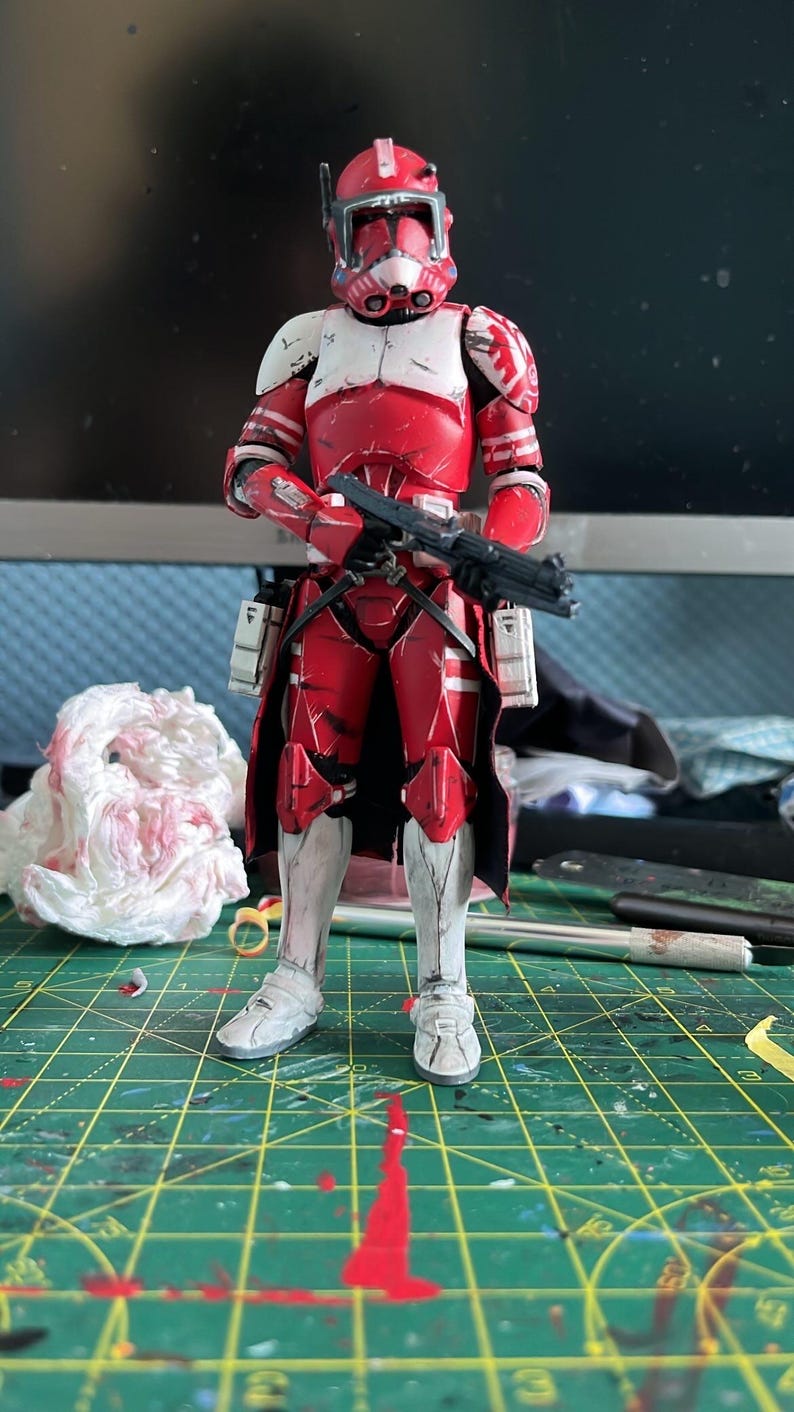 Pu&ograve; includere: Action figure rossa e bianca di un clone trooper di Star Wars. La figura &egrave; in piedi, con un fucile blaster nero. Indossa un elmetto, un'armatura e stivali. Lo sfondo &egrave; sfocato.