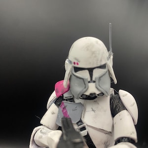 Pu&ograve; includere: Action figure bianca e grigia di un soldato con elmetto, armatura e fucile blaster. La figura ha accenti rosa sulla spalla e sul casco. La figura &egrave; in posa da battaglia, con il fucile puntato in avanti.