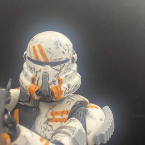 Pu&ograve; includere: Action figure dettagliata di un clone trooper di Star Wars. La figura &egrave; prevalentemente bianca con segni arancioni e dettagli usurati dalla battaglia. Il casco e l'armatura sono progettati in modo intricato.