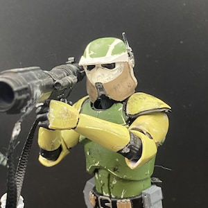 Pu&ograve; includere: Action figure dettagliata di un soldato in armatura verde e gialla, che tiene in mano una grande arma nera. L'elmetto &egrave; verde e bianco, con una copertura per il viso marrone. La figura &egrave; in posa come se stesse mirando l'arma.