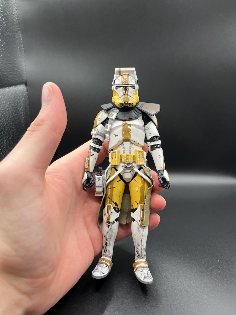 Pu&ograve; includere: Action figure dettagliata di un clone trooper di Star Wars. La figura &egrave; principalmente bianca con accenti gialli e marroni, tra cui il casco, il petto e le gambe. Ha dettagli neri e tiene un piccolo accessorio rettangolare.